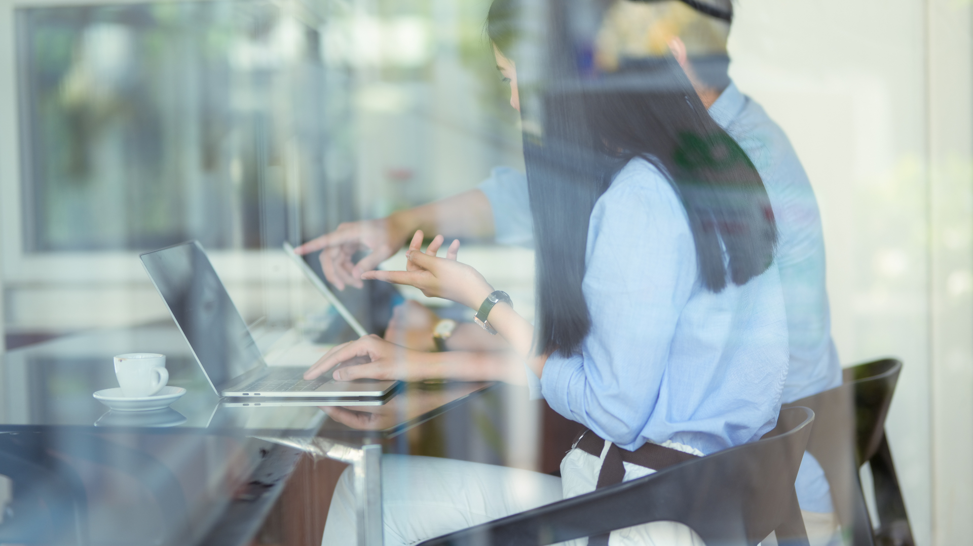 Colleagues collaborating at a glass table viewed through reflective window